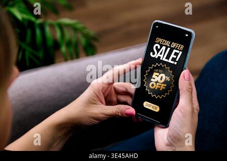 Woman using smartphone with sale advertisement on screen. Mobile ecommerce marketing and online shopping concept with discount offer and digital promo Stock Photo