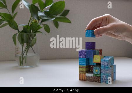 Close-up of a hand stacking colorful magnetic building blocks on a table. Educational magnetic toy for creativity, learning concept Stock Photo