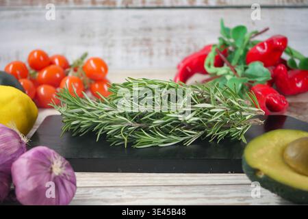 Fresh rosemary on a cutting board with various fruits and veggies Stock Photo