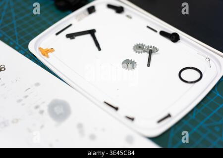 White plastic model kit parts including gears, screws, and rods arranged on tray over green cutting Stock Photo