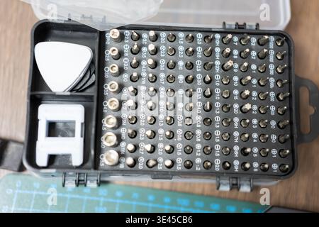Precision Screwdriver Bit Set in Black Case with Guitar Pick and Socket Adapter on Wooden Workbench Stock Photo