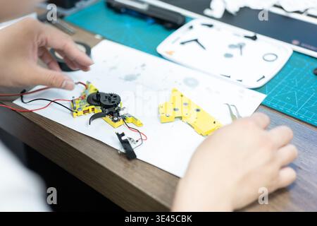 Hands assembling yellow mechanical parts with wiring on workbench in workshop, close-up view Stock Photo