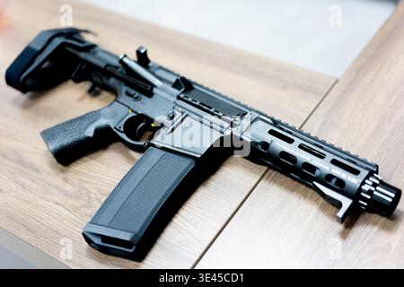 Black AR-15 style rifle with collapsible stock resting on wooden table in indoor setting Stock Photo