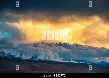 Dramatic cloud formation over mountain ranges near Mount Gongga in western China, with illuminating sunlight breaking through dense storm clouds. Stock Photo
