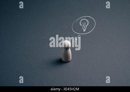 Wooden peg figure on dark gray background with a drawn lightbulb thought bubble, minimalist concept image for idea, creativity, brainstorming and busi Stock Photo