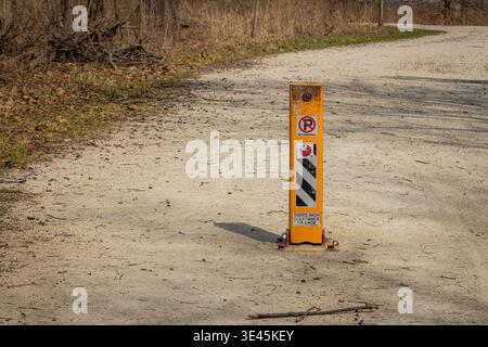 An orange safety bollard with a "No Parking" sign and reflective hazard stripes standing on a gravel path in a Naperville, Illinois forest preserve Stock Photo