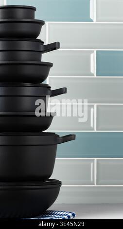 Stack of black cooking pots on a kitchen counter with blue and white tiles in the background Stock Photo