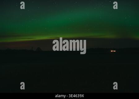 Green aurora borealis glowing above a dark rural landscape under a clear starry sky. A striking natural scene ideal for travel, science, and atmospher Stock Photo