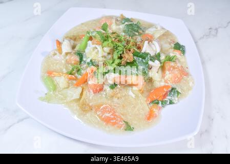 A stunning presentation of Kuey Teow Kungfu, featuring a "nest" of crispy fried flat noodles covered in a thick, translucent egg gravy with prawns, sq Stock Photo
