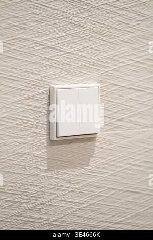 White electrical light switch with two buttons on a modern textured wall inside a house, representing home automation, energy control, and technology Stock Photo