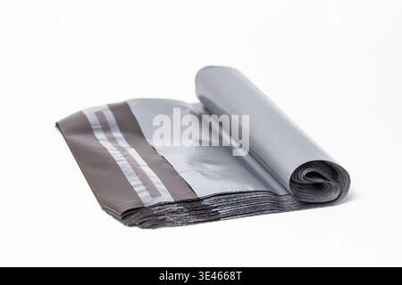 Neatly rolled stack of black poly mailer bags with self-adhesive strips, placed on a clean white background. Stock Photo