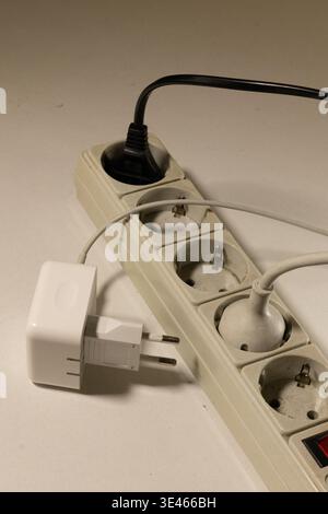Minimalist product shot of a white power adapter lying next to a beige extension cord with multiple sockets. Stock Photo