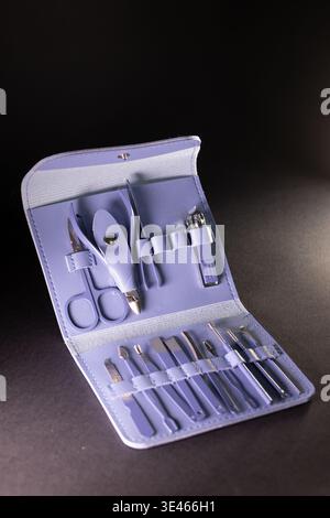 Open Violet leather case with manicure tools: scissors, clippers, files, pusher, and accessories. Metallic parts gleam under light, while soft case te Stock Photo