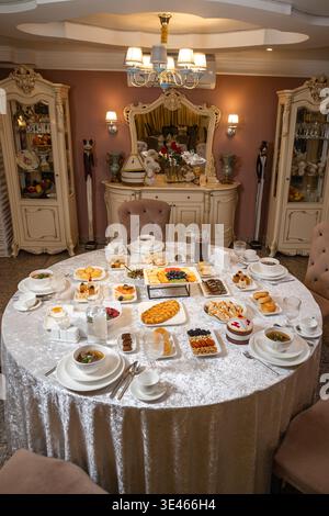 Elegantly set round festive table covered with a luxurious silver tablecloth, richly laden with traditional Kazakh national dishes, appetizers, soups, Stock Photo