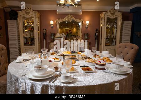 Elegantly set round festive table covered with a luxurious silver tablecloth, richly laden with traditional Kazakh national dishes, appetizers, soups, Stock Photo