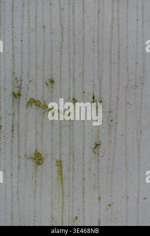 Close up of weathered wall surface with vertical stripes, stains and green moss patches. Stock Photo