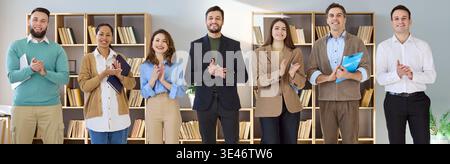 Smiling business team applauding at office meeting, standing together in workspace Stock Photo