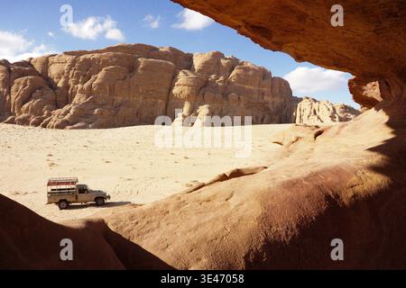 Four wheel drive safari vehicle driving across sandy desert landscape surrounded by large sandstone rock formations under clear blue sky. Stock Photo