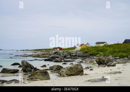 Rocky coastal shoreline with scattered houses overlooking calm sea under overcast sky along a rural seaside landscape. Stock Photo