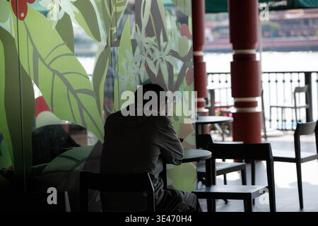 Man sitting and relaxing, using smartphone, casual phone use outdoors, relaxed digital moment, rear view, at Tha Maharaj. Stock Photo