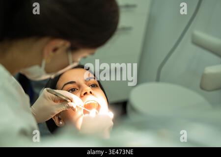 Dentist performing oral care on a female patient in a modern clinic Stock Photo