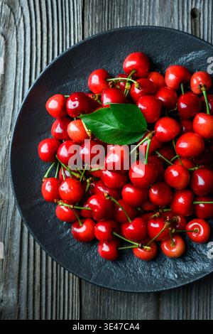 Top view of cherries arranged in black plate on wooden table. Fresh organic sweet fruit, minimal rustic styling Stock Photo
