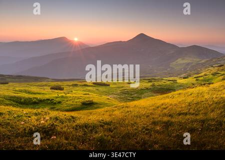 Incredible sunset with golden sunlight casting a warm glow over lush grassy meadows in the summer mountains. Landscape photography Stock Photo