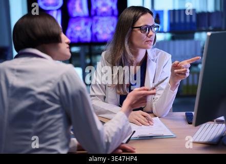 Two doctors collaborate in a modern workspace, discussing patient data and brain scans in a bright, high-tech environment Stock Photo