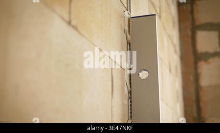 A worker uses a level to check the wall. The man uses a level with his hands and measures the vertical surface of the wall. Close-up. Preparing for ho Stock Photo