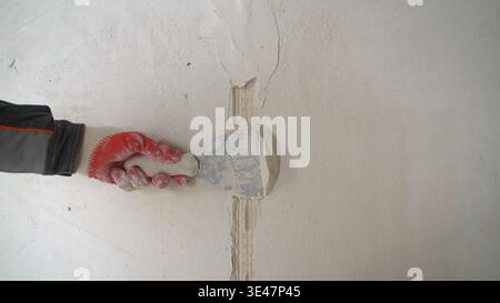 Construction worker's hand in a glove using a putty knife to apply plaster and fill a crack in a wall. Stock Photo