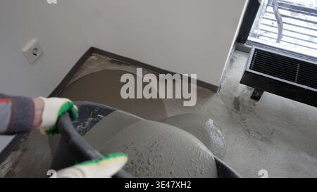 Worker pouring self leveling screed on concrete floor during renovation. Stock Photo
