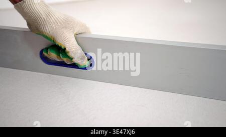 Builder in a work glove uses a spirit level tool on a fresh white plaster wall. Stock Photo