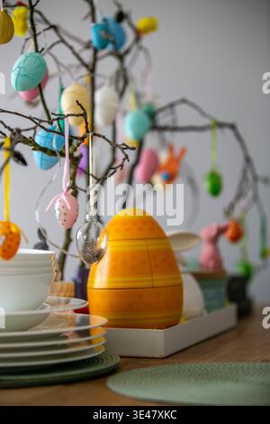 Festive Easter tree and table decoration with pastel eggs and bunny ornaments above a table set with white plates and a large yellow decorative egg Stock Photo
