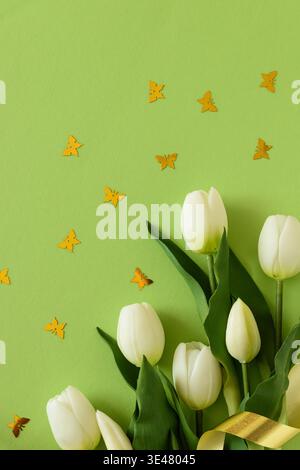 Elegant spring composition featuring white tulips arranged with butterflies confetti on a soft green background with a flowing satin ribbon. Easter or Stock Photo