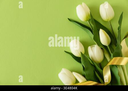 Elegant spring composition featuring white tulips arranged on a soft green background with a flowing satin ribbon. Easter or Mothers Day celebration Stock Photo
