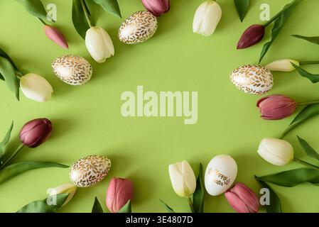 Festive spring flat lay featuring pastel Easter eggs arranged in a circular frame surrounded by white and deep purple tulips on a bright green backgro Stock Photo