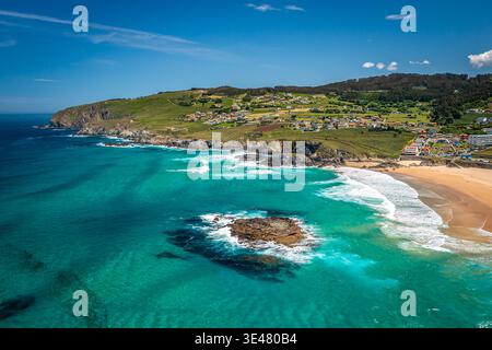 Aerial coastal panorama showing turquoise ocean waves breaking onto a wide golden sand beach, Valdovino, Spain Stock Photo