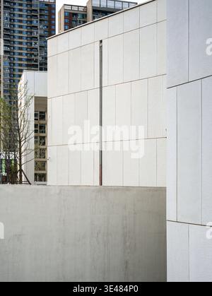 Minimalist white concrete building facade featuring a single vertical pipe set against a modern urban residential background. The scene represents con Stock Photo