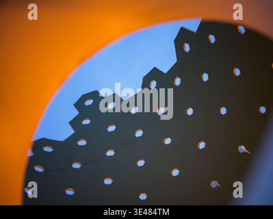 Close up of an abstract perforated metal architectural structure with hexagonal patterns against a vibrant contrasting orange and blue background. The Stock Photo