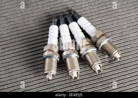 Four new car spark plugs. Features white ceramic insulator, metallic body, threaded electrode. Essential for engine ignition, ready for automotive rep Stock Photo