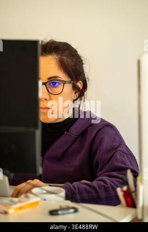 A woman looks at a computer screen with a concentrated expression while in smart work. The woman is thirty-nine years old Stock Photo
