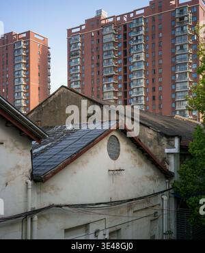 Old traditional white houses with dark pitched roofs standing in sharp contrast against modern high-rise residential towers under a blue sky. The scen Stock Photo