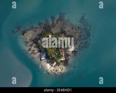 Aerial view of a small tropical island with lush vegetation, a red-roofed building, and a sandy beach surrounded by turquoise water in Bijagos, Guinea Stock Photo