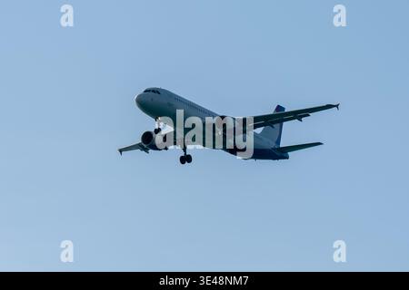Commercial airliner descends with landing gear extended against a clear blue sky during final approach, illustrating modern aviation, passenger travel Stock Photo