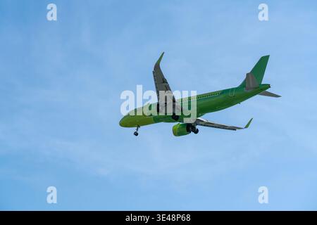Bright green passenger airplane descends for landing against a clear blue sky, with landing gear and winglets visible; a modern commercial aviation sc Stock Photo