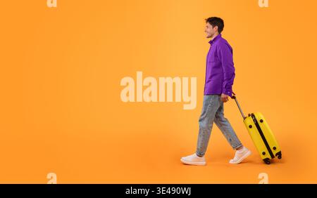 Man Walks With Yellow Suitcase Against Orange Background in Bright Setting Stock Photo