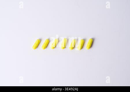 Seven yellow capsules arranged in a row on a white background, simple medication concept with copy space. Stock Photo