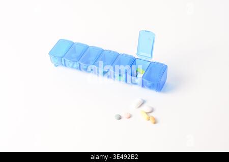 Blue pill organizer with one open compartment and assorted pills on a white background, medication management concept. Stock Photo