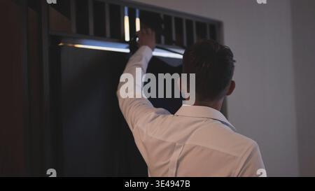 Rear view of a groom in a white dress shirt getting his suit jacket from a dark wardrobe. Stock Photo