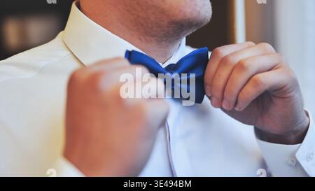 Close up of a man in a white dress shirt adjusting his royal blue bow tie. Stock Photo